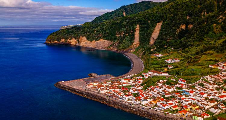 Kustdorpje met kleurrijke daken verscholen onder weelderige vulkanische rotswanden op het eiland São Miguel.