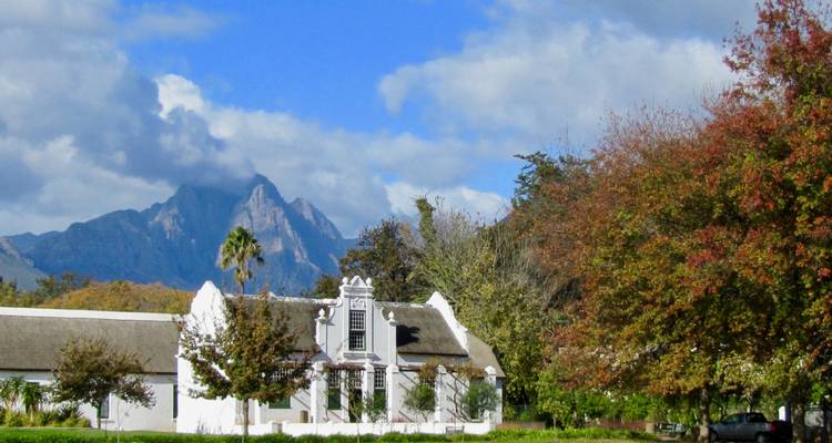 White Cape Dutch manor house framed by autumn trees with mountains in the background