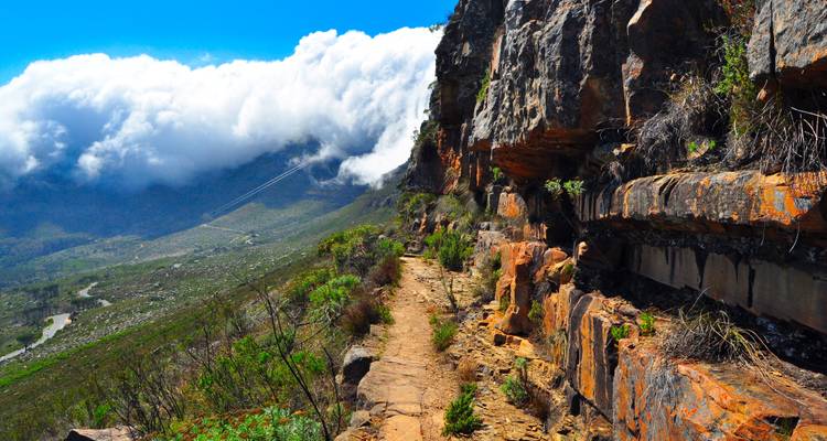 Rocky mountain path with sheer orange cliffs and rolling clouds in the valley below