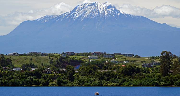 Paysage de montagne enneigée avec des maisons dispersées sur une colline verte.