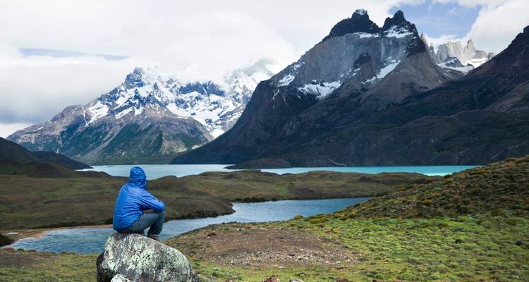 Personne en veste bleue observant des montagnes enneigées de l'autre côté d'un lac.