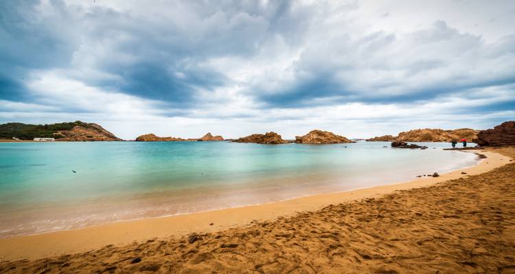Une plage avec des eaux turquoise sous un ciel nuageux.