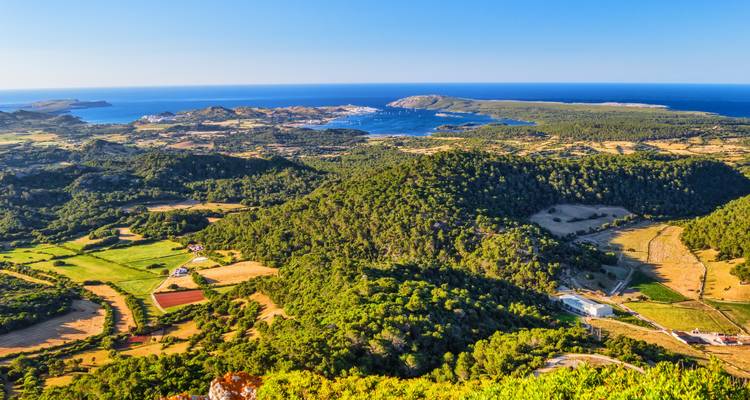 Erhaben gelegener Aussichtspunkt über Menorcas sanft hügelige grüne Landschaft und blaue Buchten, die sich bis zum Horizont ausbreiten.