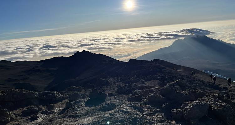 Breathtaking view from a mountain peak above the clouds with the sun in the sky.