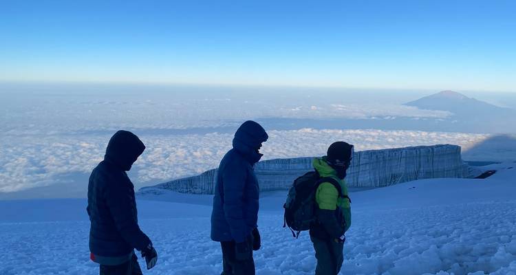 People hiking on a snowy path above the clouds.