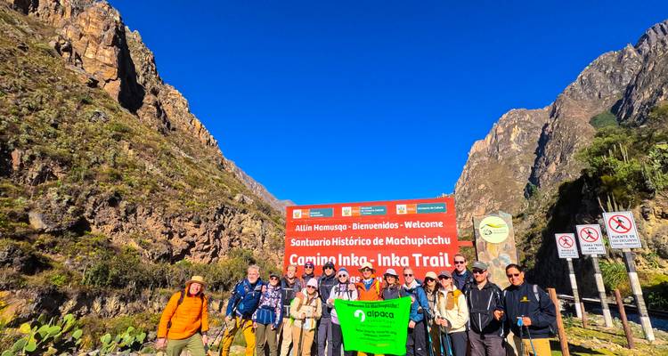 Groupe de randonneurs posant devant un panneau du Chemin de l'Inca, entourés de montagnes.