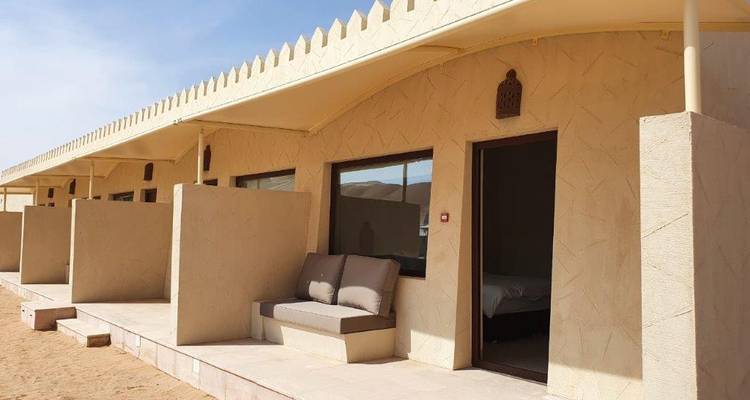 Alojamiento en el desierto con paredes beige y asientos exteriores sencillos.