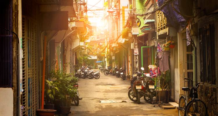 Callejón urbano con mucho ambiente lleno de motos, plantas e iluminado por la luz dorada de la hora mágica en Ho Chi Minh City