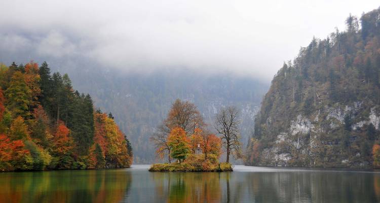 Una pequeña isla con árboles otoñales en un lago de montaña reflectante.