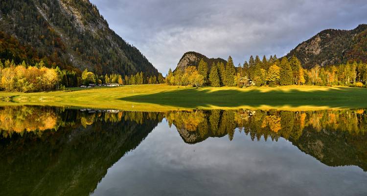 Un paisaje sereno con el reflejo de una pradera y bosque, rodeado de montañas.