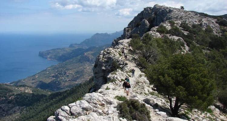 Hikers walking along a rocky ridge with ocean views in the background.