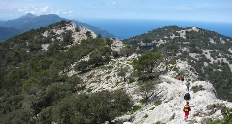 Several hikers walking along a rocky mountain ridge with sea views.