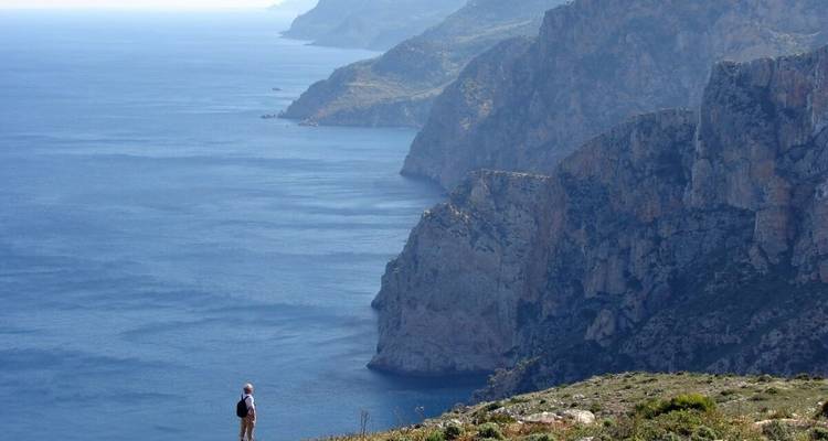 A person standing on a cliff overlooking the sea with steep rock formations.