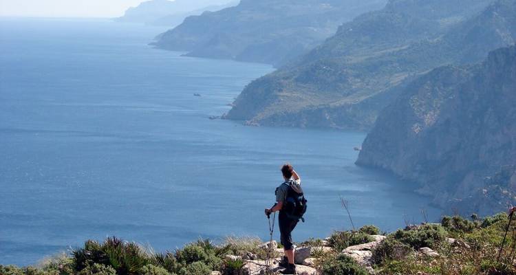 A hiker with a backpack standing on a cliff overlooking the sea.