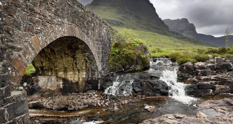 Stone bridge over a stream in a mountainous landscape.