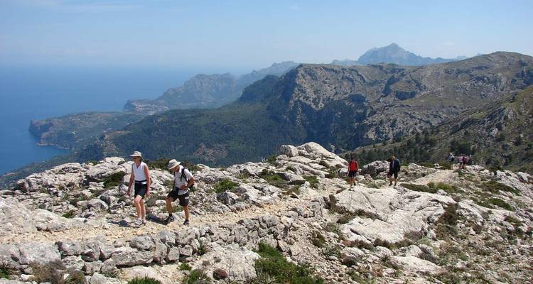 Des randonneurs marchant sur un sentier rocheux avec une vue sur la mer et les montagnes.
