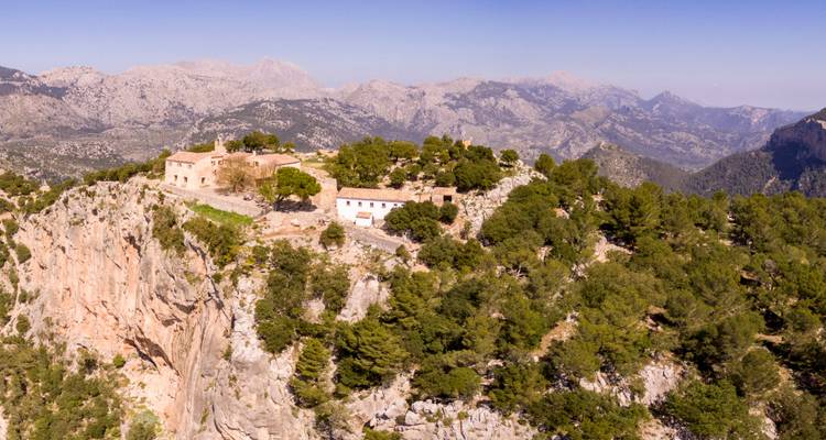 Abgelegener Klosterkomplex auf einer Klippenkante gelegen, umgeben von Kiefernwäldern und dunstige Berglandschaften.