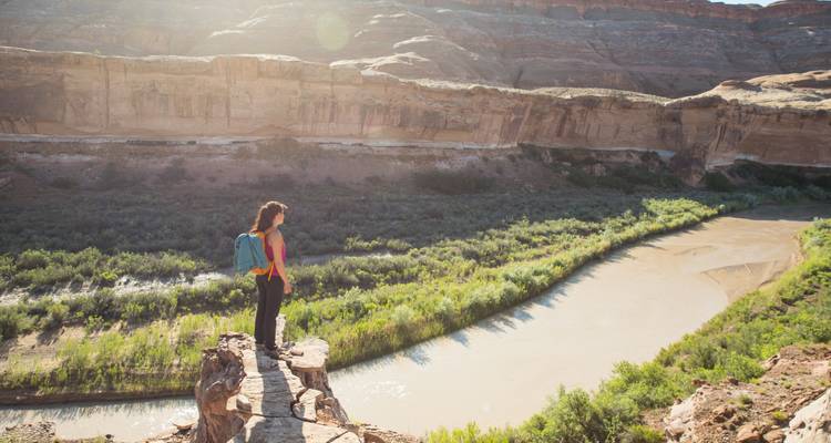 Eine Frau, die auf einer Klippe steht und auf einen Fluss in einem Canyon blickt.