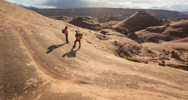 Zwei Wanderer stehen auf einem Felsvorsprung mit einer Schlucht in der Ferne.