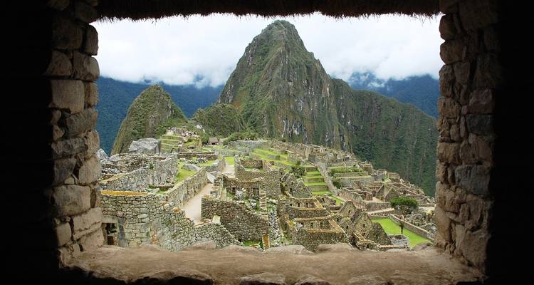 Zicht op de ruïnes van Machu Picchu vanuit een opening in een stenen gebouw.