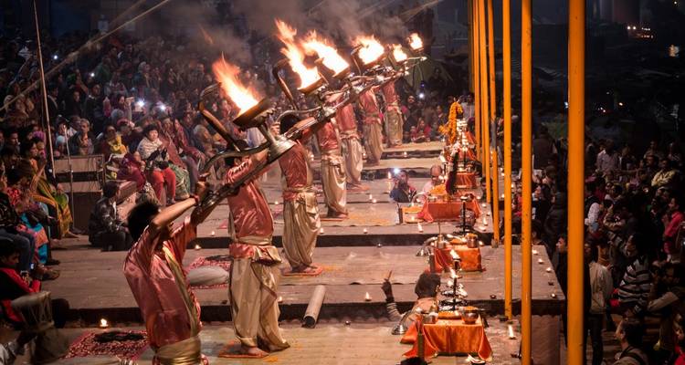 Ritual nocturno con sacerdotes sosteniendo lámparas de fuego sobre un río.