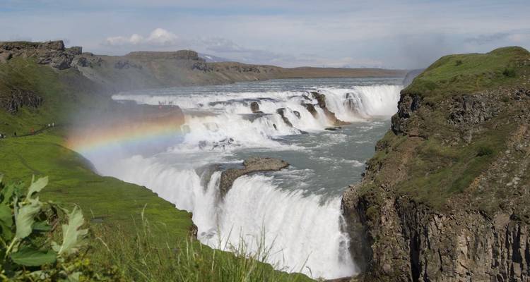 Gullfoss waterfall with a colorful rainbow and lush green cliffs.