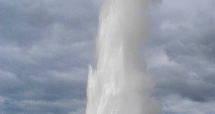 Powerful geyser erupting with cloudy sky backdrop.