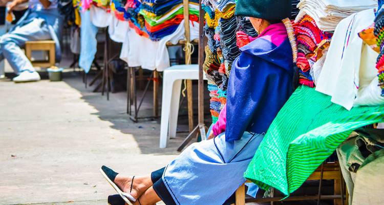 Marché textile coloré avec une personne assise parmi les tissus vibrants.