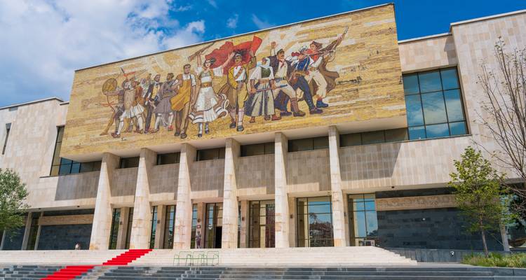 Grand bâtiment avec une fresque murale et des marches au premier plan.
