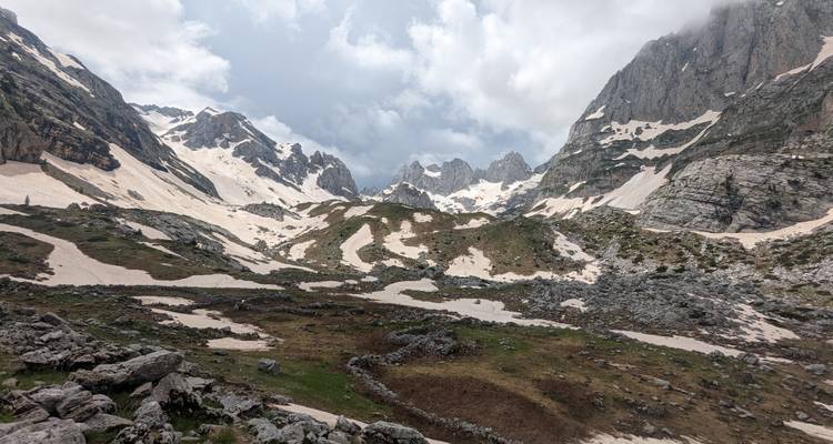 Montagnes enneigées avec un ciel nuageux surplombant un terrain rocheux.