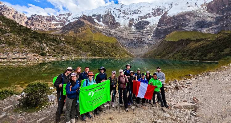 Groep wandelaars bij een schilderachtig bergmeer met besneeuwde bergen.