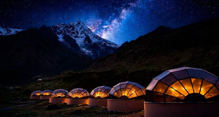 Fila de cúpulas de vidrio iluminadas bajo un cielo lleno de estrellas y picos andinos cubiertos de nieve.