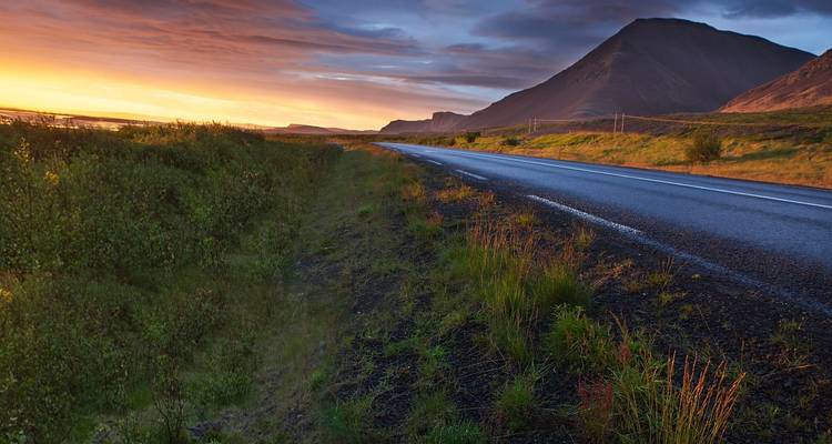 Schilderachtige weg bij zonsondergang met bergen op de achtergrond.