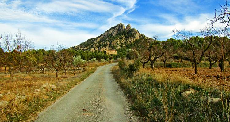 Ein ländlicher Weg, der zu einem dramatischen Felsenhügel unter klarem Himmel führt.