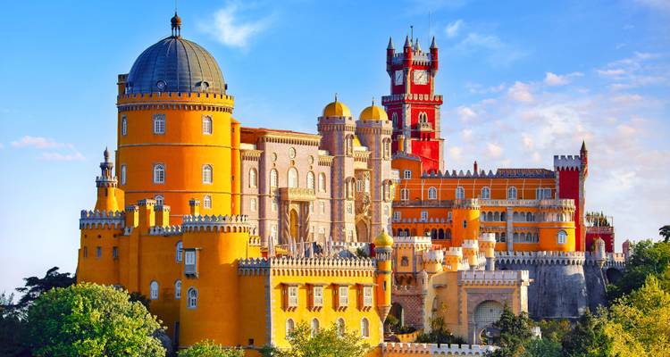 El Palacio da Pena con sus colores vibrantes encaramado en lo alto de una colina exuberante en Sintra contra un suave cielo vespertino.