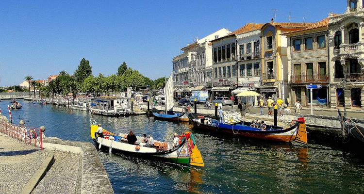 Barcas coloridas parecidas a góndolas navegando por el canal de Aveiro junto a edificios Art Nouveau ornamentados en un día soleado.