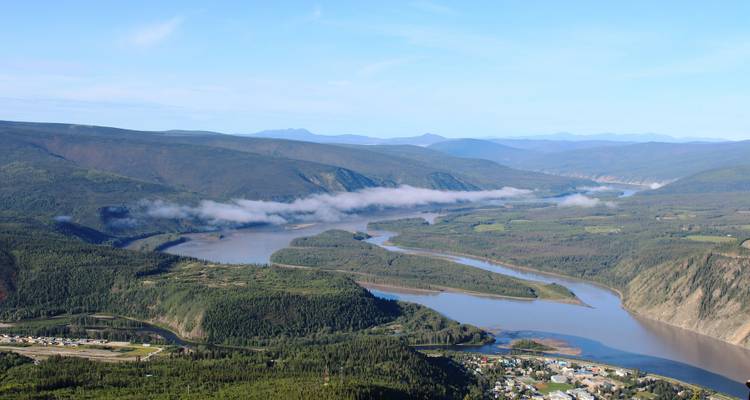 Rivière serpentant à travers une vallée luxuriante avec des montagnes en arrière-plan.