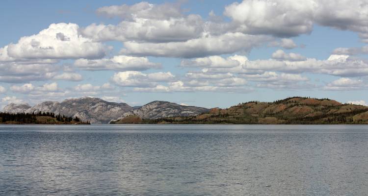 Lac calme avec des montagnes et un ciel partiellement nuageux.