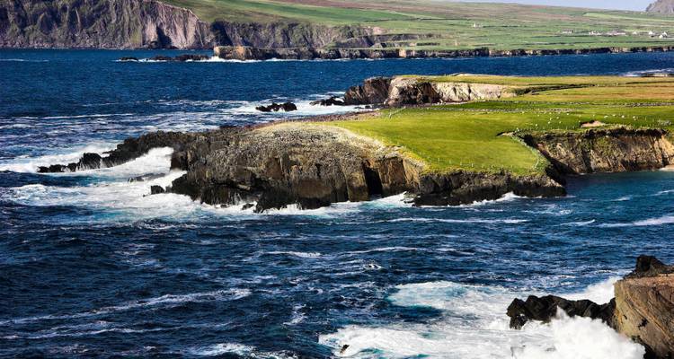 Costa atlántica accidentada con olas que se estrellan contra acantilados rocosos y promontorios verdes.