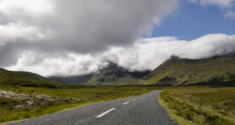Carretera en páramo abierto que se extiende hacia picos envueltos en niebla con nubes bajas rodando sobre las cimas.