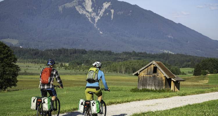 Two cyclists riding on a path with mountains in the background.