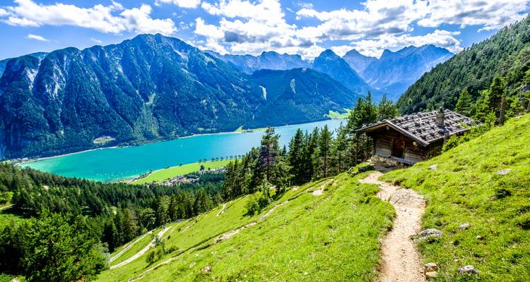 Scenic view of a lake with mountains and a wooden cabin in the foreground.