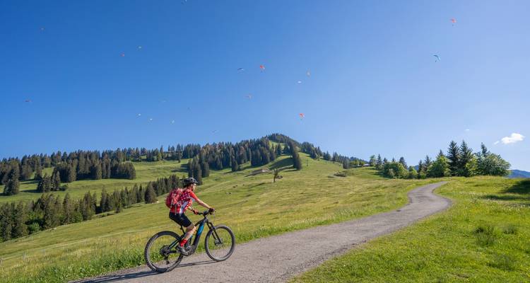 Cycliste sur une route avec des parapentes colorés parsemant le ciel.