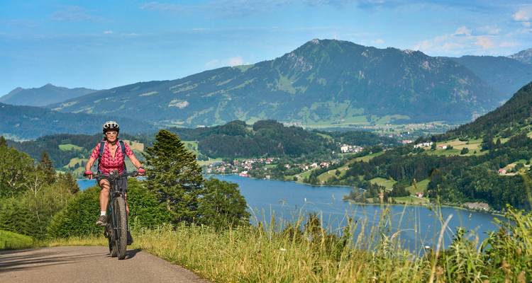 A person biking on a road overlooking a lake and mountains.