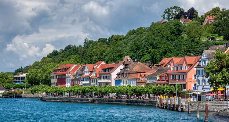 Rangée de maisons et de cafés aux couleurs vives alignés le long d'une promenade verdoyante au bord du lac.