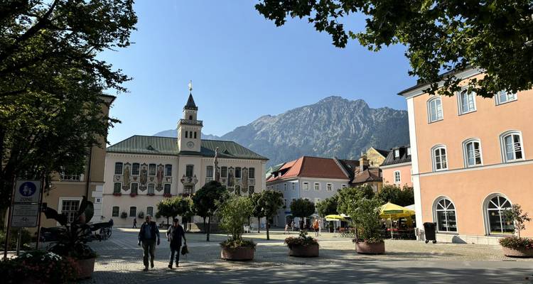 Place de ville avec bâtiments historiques et montagnes en arrière-plan.
