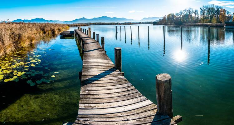 Jetée en bois s'étendant dans un lac calme avec des montagnes au loin.