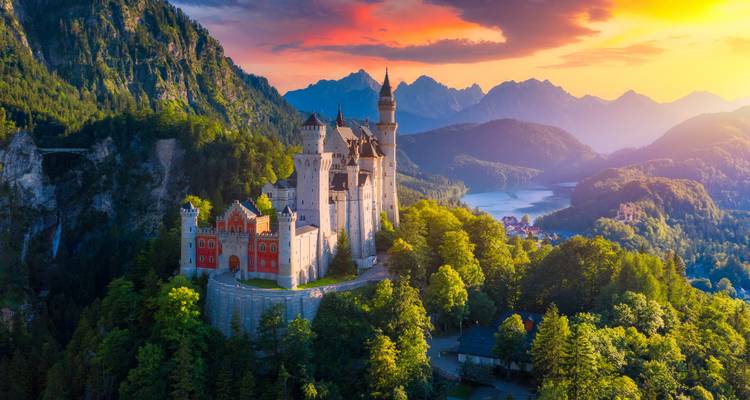 Neuschwanstein Castle with snowy mountains at sunset.