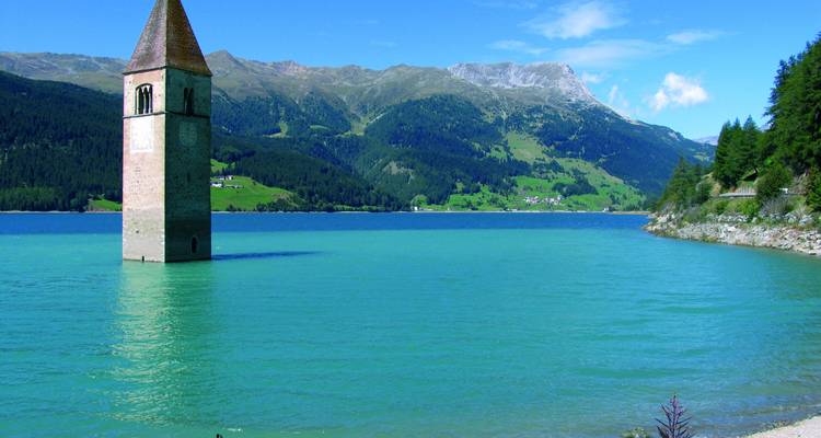 Historische kerktoren komt uit het turquoise alpenmeer tevoorschijn, omgeven door bergen