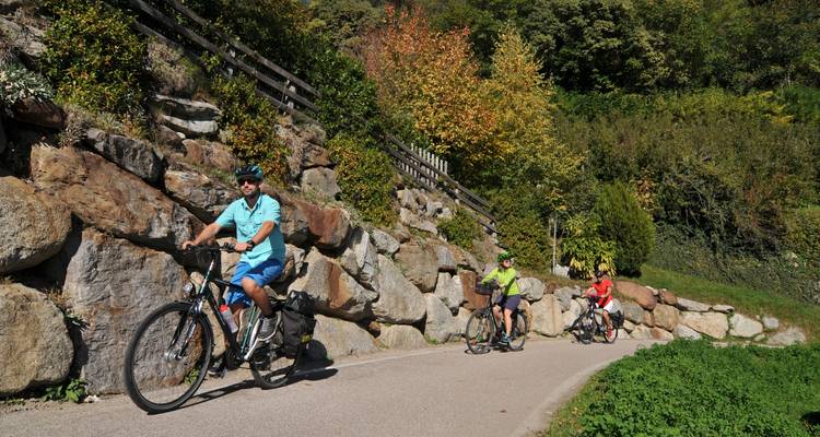 Fietsers trappen langs een schaduwrijk landswegetje met aan beide zijden grote rotswanden en herfstkleuren